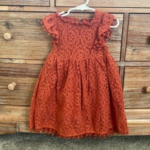 Toddler burnt orange lace dress with pom pom edging.